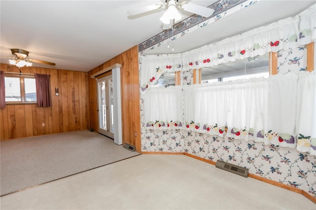 interior space with carpet floors, wooden walls, visible vents, and a ceiling fan