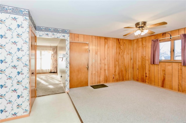 carpeted spare room with ceiling fan, wood walls, and a wealth of natural light