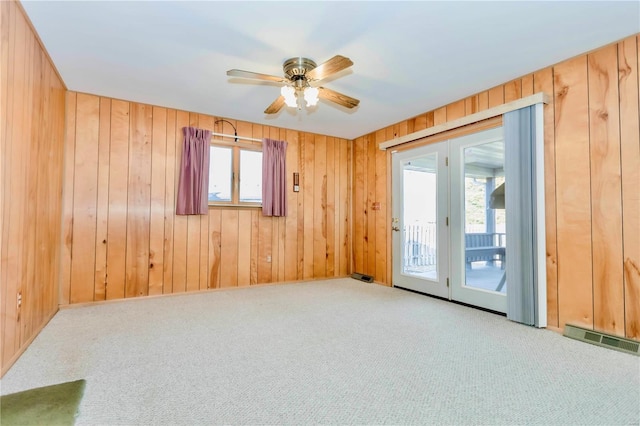 carpeted empty room featuring wood walls, plenty of natural light, visible vents, and a ceiling fan