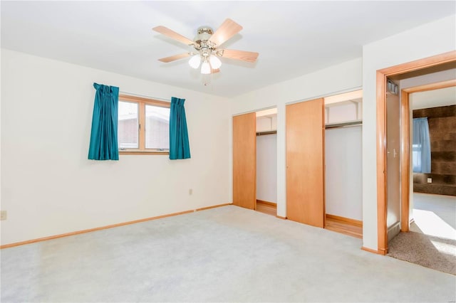 unfurnished bedroom with carpet floors, a ceiling fan, baseboards, and multiple closets