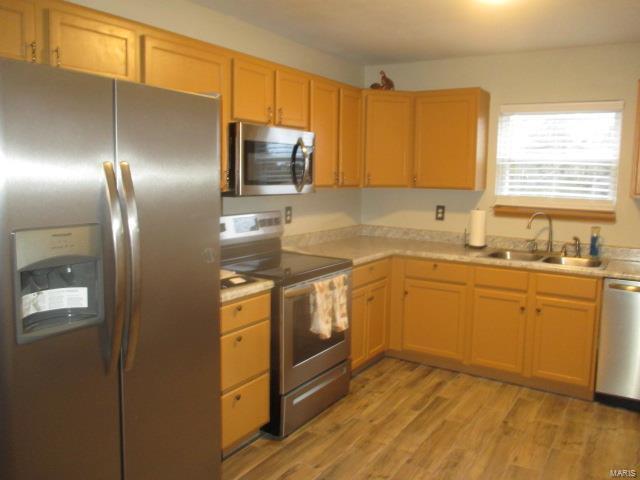 kitchen featuring stainless steel appliances, light wood-style floors, light countertops, and a sink