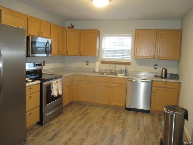 kitchen featuring stainless steel appliances, light wood-type flooring, light countertops, and a sink