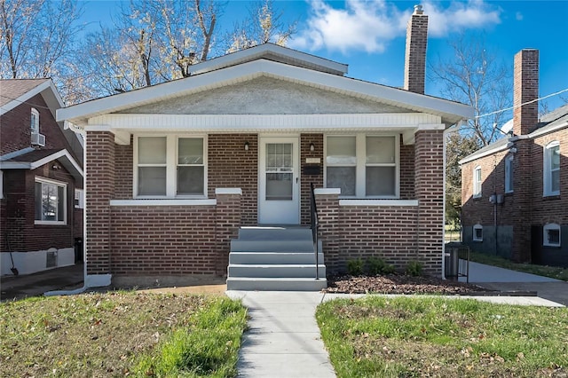 bungalow-style home with covered porch, brick siding, and a chimney