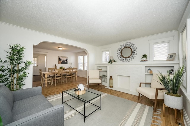 living area featuring a textured ceiling, arched walkways, wood finished floors, and ornamental molding