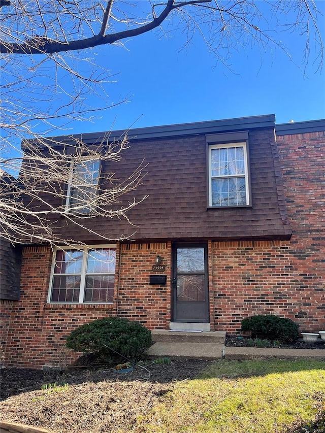 view of front of home with a shingled roof, brick siding, and mansard roof