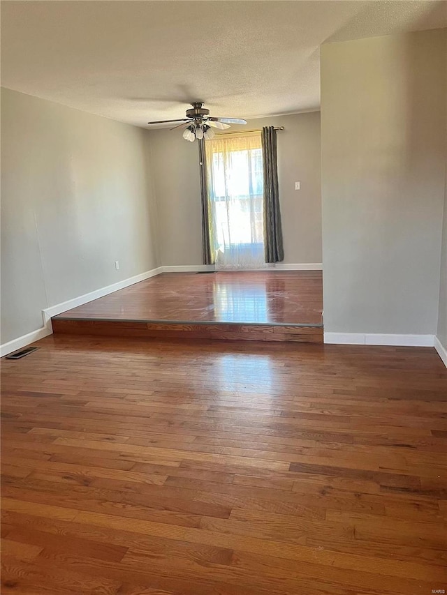 unfurnished room with a textured ceiling, wood finished floors, visible vents, a ceiling fan, and baseboards