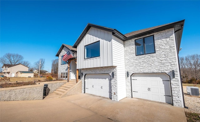 view of front facade with an attached garage, board and batten siding, central AC, stone siding, and driveway