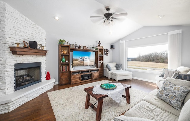 living room with dark wood-style floors, vaulted ceiling, a stone fireplace, and baseboards