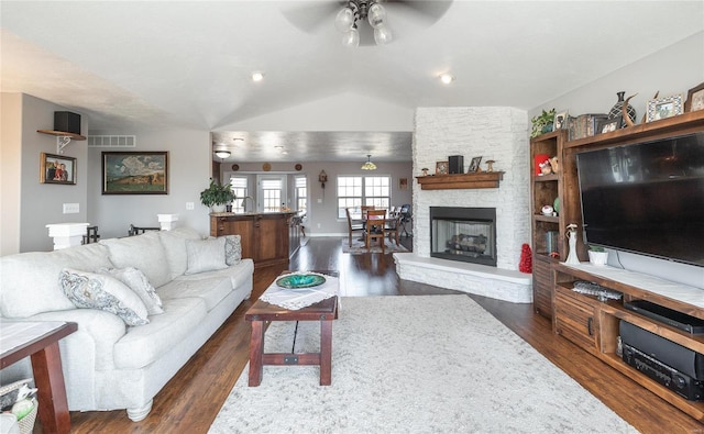 living area with visible vents, dark wood finished floors, lofted ceiling, ceiling fan, and a stone fireplace