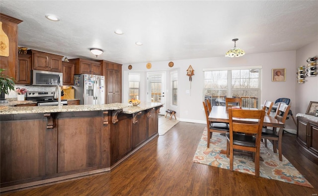 kitchen featuring dark wood-style flooring, appliances with stainless steel finishes, light stone countertops, a peninsula, and a kitchen bar