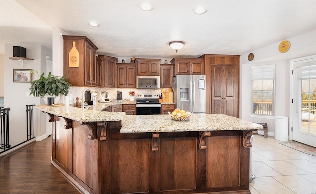 kitchen featuring appliances with stainless steel finishes, a breakfast bar, a peninsula, and light stone countertops