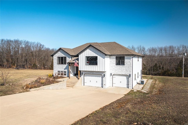 bi-level home with board and batten siding, central AC, a garage, stone siding, and driveway