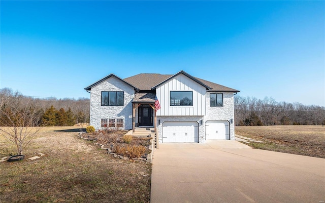 split foyer home with a garage, concrete driveway, stone siding, roof with shingles, and board and batten siding