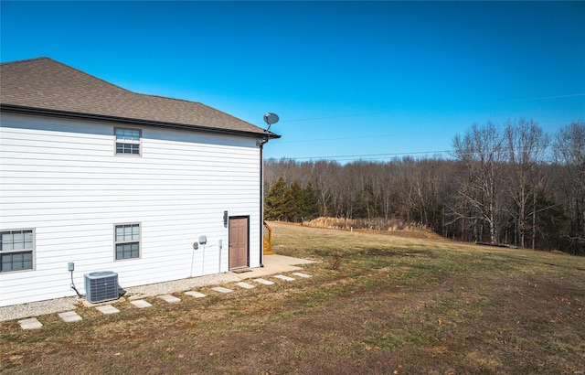 view of property exterior featuring a shingled roof, central AC unit, and a yard