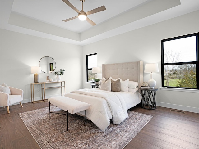 bedroom with baseboards, visible vents, a raised ceiling, and wood finished floors