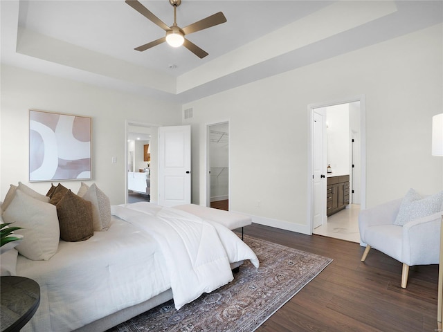 bedroom featuring baseboards, visible vents, wood finished floors, a spacious closet, and a tray ceiling