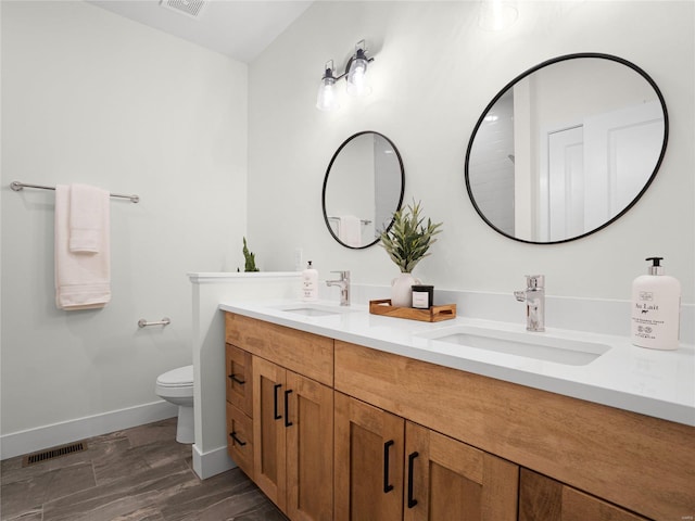 bathroom with toilet, double vanity, baseboards, and a sink