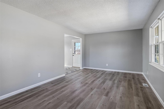 empty room featuring a textured ceiling, wood finished floors, visible vents, and baseboards