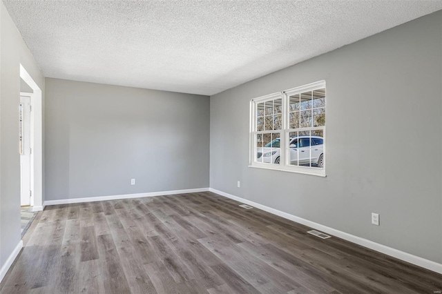 empty room with a textured ceiling, wood finished floors, visible vents, and baseboards