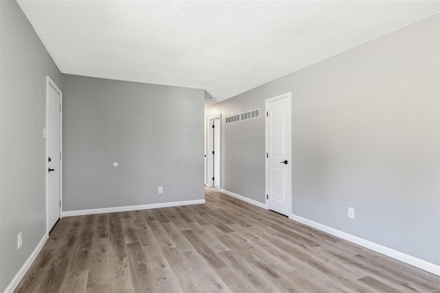 spare room with a textured ceiling, baseboards, and wood finished floors