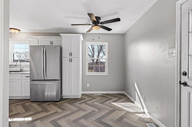 kitchen with a healthy amount of sunlight, white cabinetry, a sink, and freestanding refrigerator