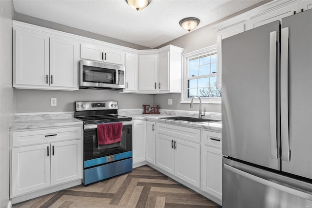 kitchen with a textured ceiling, stainless steel appliances, a sink, and white cabinets