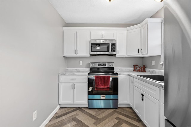 kitchen featuring stainless steel appliances, white cabinetry, a sink, and baseboards