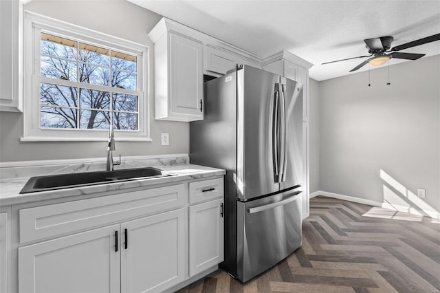 kitchen with light countertops, freestanding refrigerator, white cabinetry, a sink, and ceiling fan