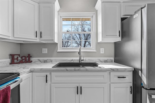 kitchen with white cabinets, a sink, and freestanding refrigerator