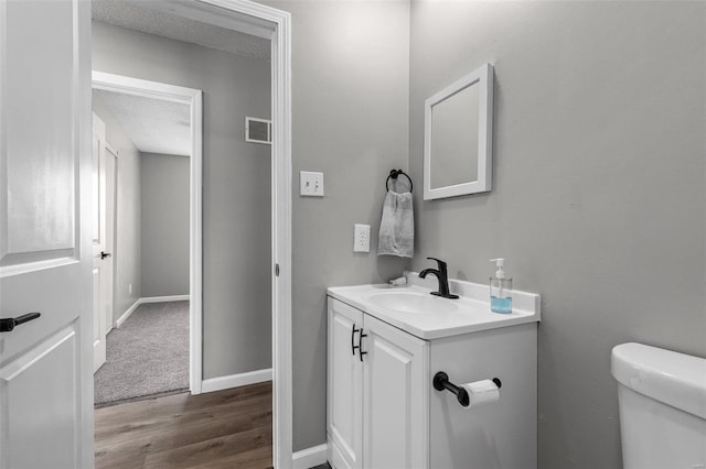 bathroom featuring baseboards, visible vents, toilet, wood finished floors, and vanity