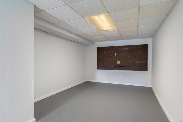 spare room with a drop ceiling, finished concrete flooring, and baseboards