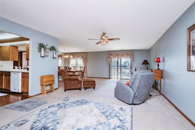 carpeted living area featuring ceiling fan with notable chandelier, baseboards, and a sink