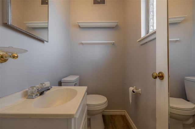 half bathroom featuring toilet, wood finished floors, visible vents, vanity, and baseboards