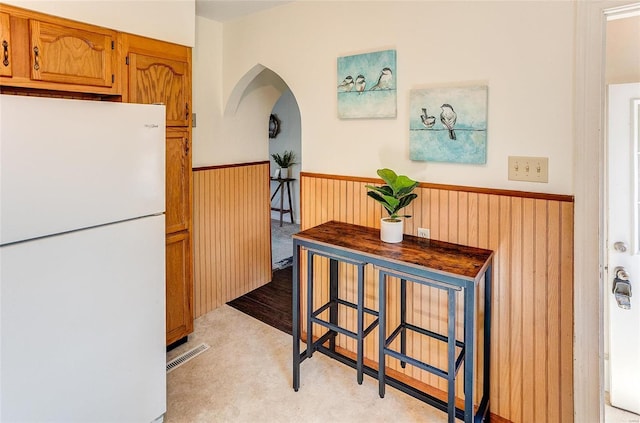 kitchen featuring a wainscoted wall, wood walls, visible vents, freestanding refrigerator, and brown cabinetry