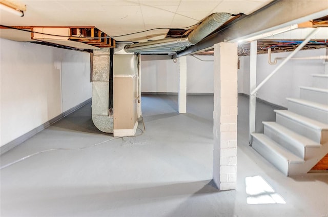 unfinished basement with baseboards, stairs, and heating unit