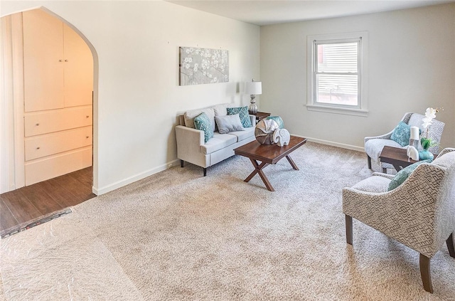 carpeted living room featuring baseboards and arched walkways