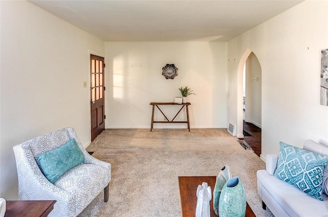 living area with carpet floors, arched walkways, visible vents, and baseboards