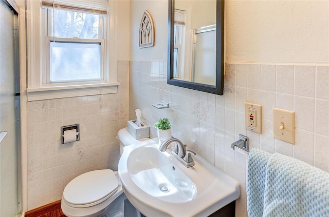 bathroom featuring a shower with shower door, a sink, toilet, and tile walls