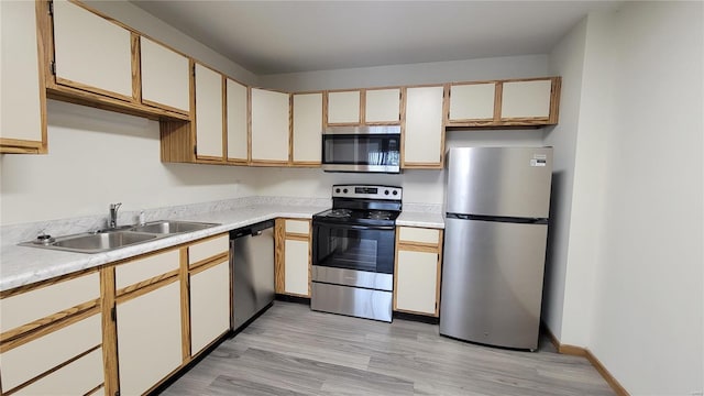 kitchen featuring light countertops, appliances with stainless steel finishes, a sink, light wood-type flooring, and baseboards