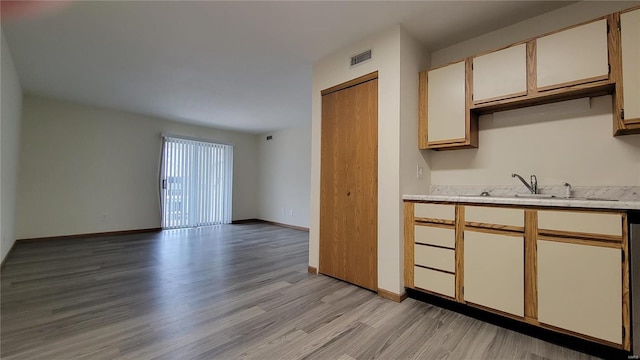 kitchen with light wood finished floors, visible vents, baseboards, light countertops, and a sink