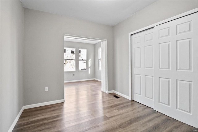 unfurnished bedroom featuring baseboards, a closet, visible vents, and wood finished floors