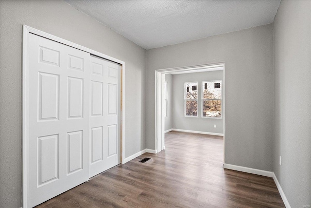 interior space with dark wood-style floors, a closet, visible vents, a textured ceiling, and baseboards