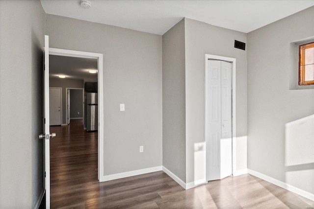 unfurnished bedroom with a closet, wood finished floors, freestanding refrigerator, and baseboards