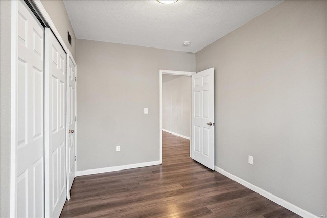 unfurnished bedroom with dark wood-style floors, a closet, a textured ceiling, and baseboards