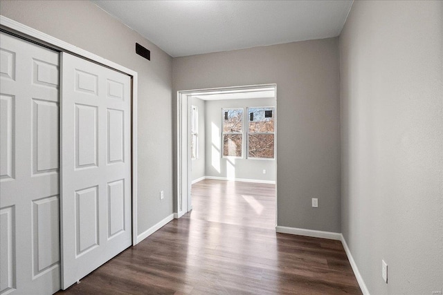 unfurnished bedroom with dark wood-style floors, a closet, visible vents, and baseboards