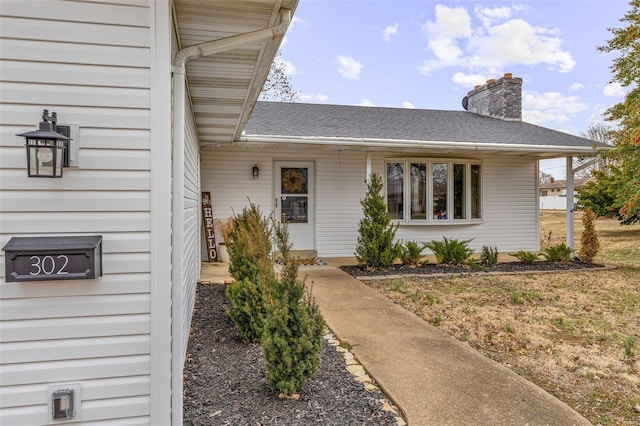 doorway to property featuring a shingled roof and a chimney