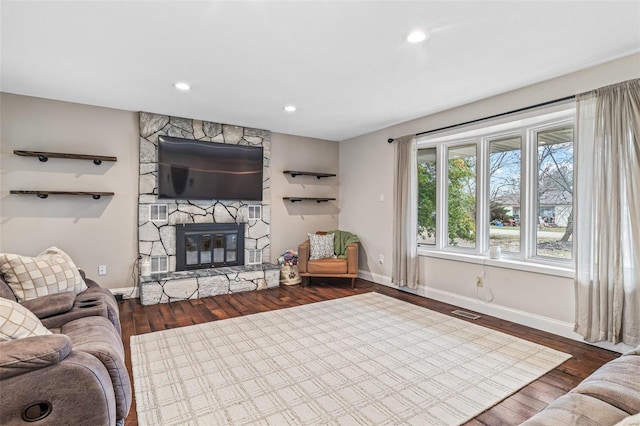 living room with visible vents, a fireplace, baseboards, and wood finished floors