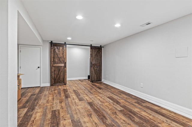 unfurnished room featuring a barn door, baseboards, visible vents, wood finished floors, and recessed lighting