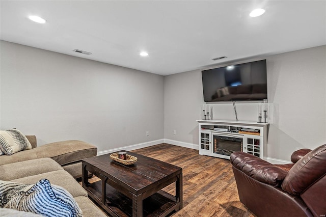 living room with a glass covered fireplace, visible vents, baseboards, and wood finished floors