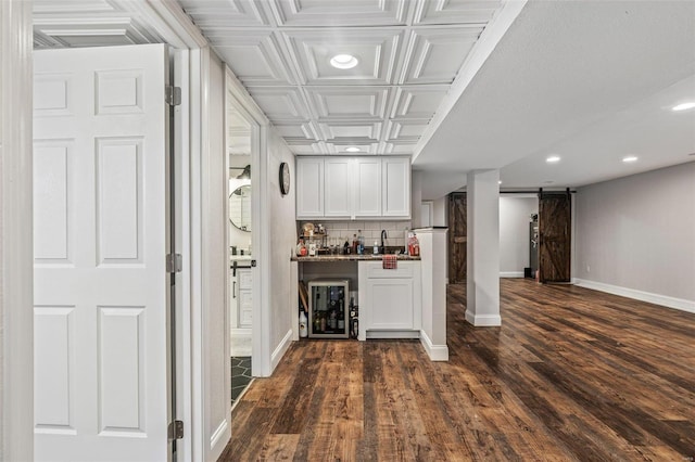 bar featuring dark wood-style floors, a barn door, baseboards, and decorative backsplash